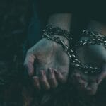 A dramatic close-up image of hands bound by silver chains, symbolizing captivity or struggle.