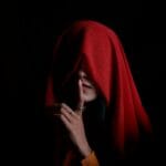 Silent Treatment Abuse: Why It Hurts and How to Respond 1 Mysterious woman in a red hood, finger on lips for silence, against a dark background.