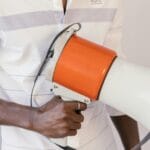 Smear Campaign After a Breakup: Why Toxic Exes Lie 2 Close-up of a person holding a megaphone, promoting voting awareness, with a 'Vote' sticker on the shirt.